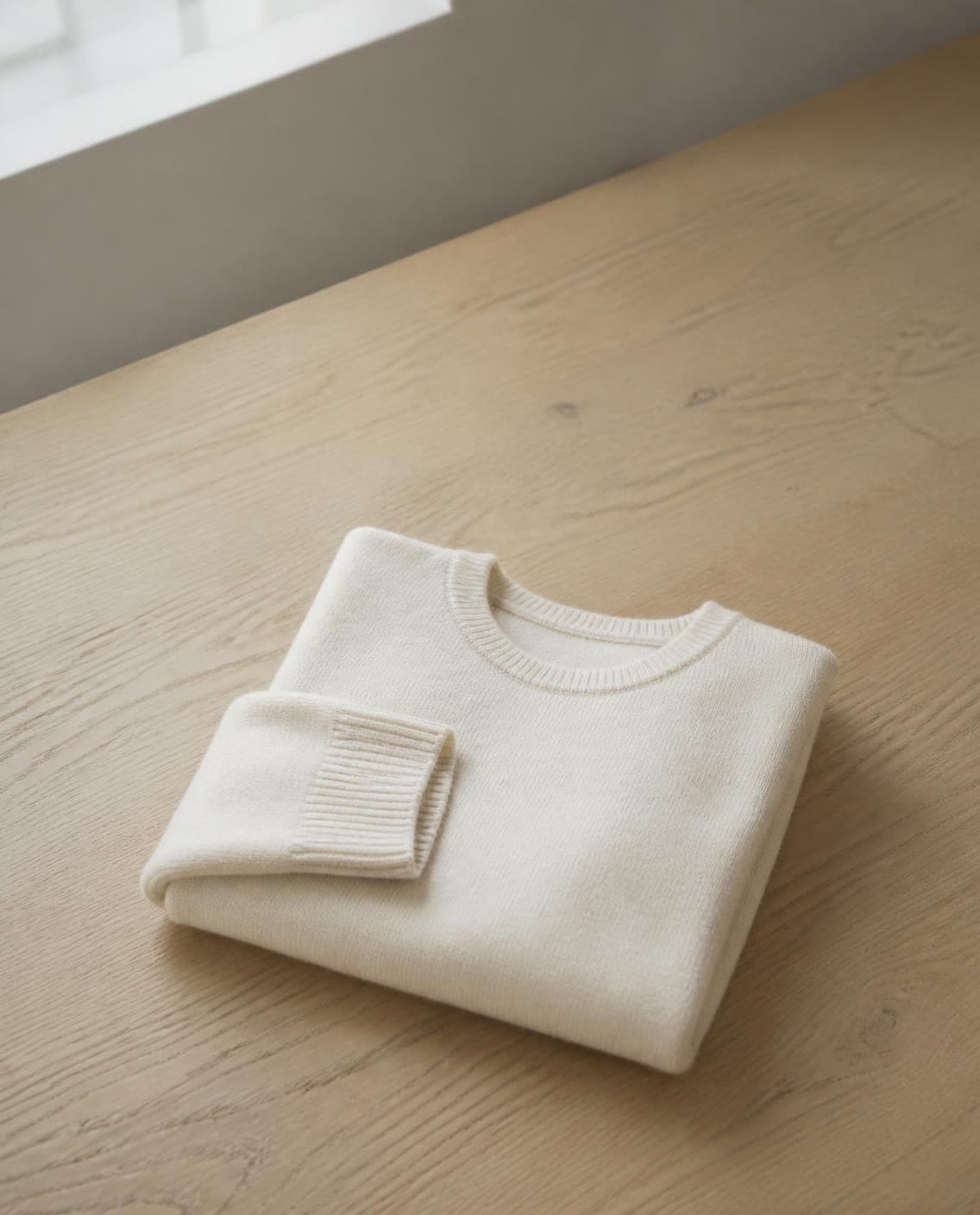 A folded cream knit sweater on an oak table (a generated photo)